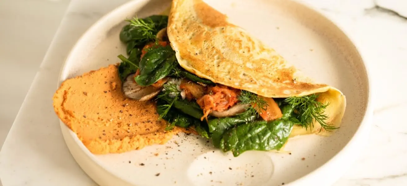 Vegetable-stuffed omelette with a side of sweet potato mash on a white plate